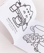 Coloring Book is opened to two white coloring pages with black graphics. On the left page is Pusheen the Cat sitting behind coffee brewing accessories and a latte cup. The text below the graphic says “Design your own latte art! Design your own lattes on the next page any way you like!” On the righthand page is Pusheen as six madeleines sitting in front of two coffee mugs with areas for the user to draw their own latte art atop the mug’s surface.  