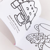 Coloring Book is opened to two white coloring pages with black graphics. On the left page is Pusheen the Cat sitting behind coffee brewing accessories and a latte cup. The text below the graphic says “Design your own latte art! Design your own lattes on the next page any way you like!” On the righthand page is Pusheen as six madeleines sitting in front of two coffee mugs with areas for the user to draw their own latte art atop the mug’s surface.  