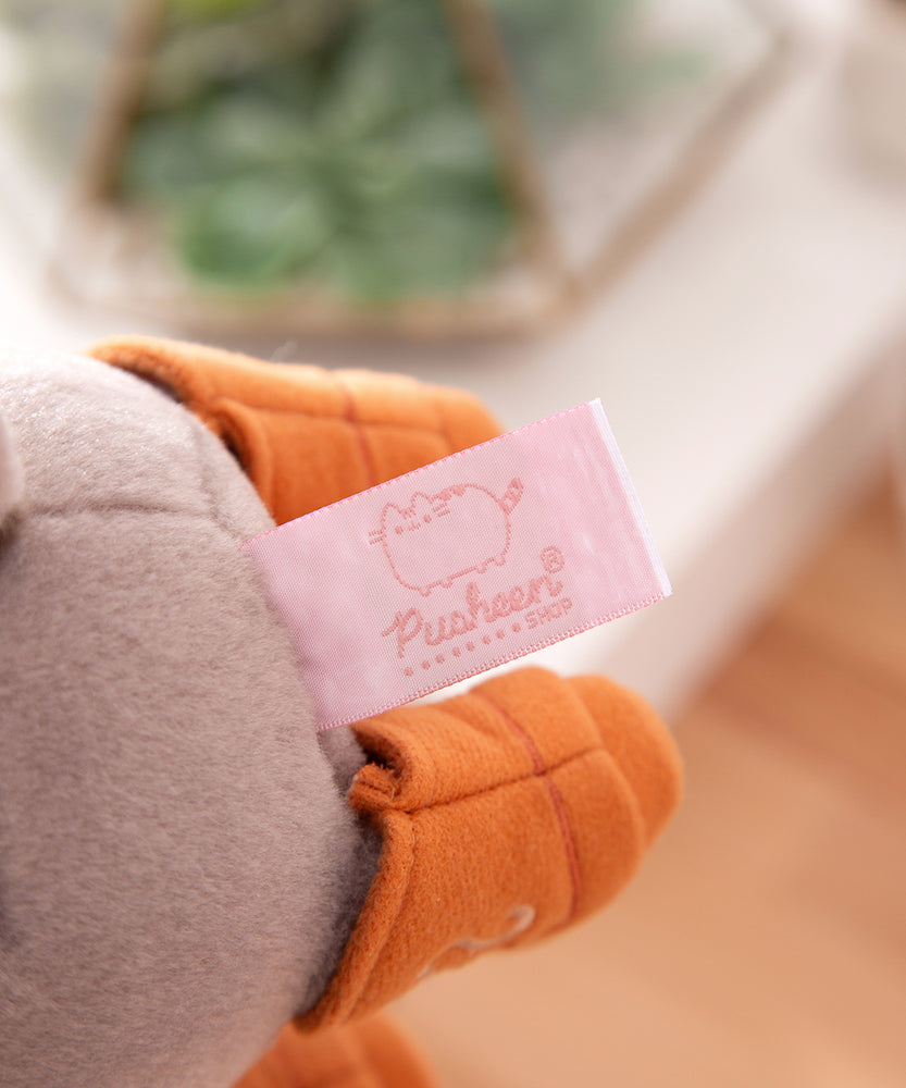 Close-up view of the cggcw logo tag that is affixed near the bottom of the grey plush.