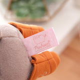 Close-up view of the cggcw logo tag that is affixed near the bottom of the grey plush.
