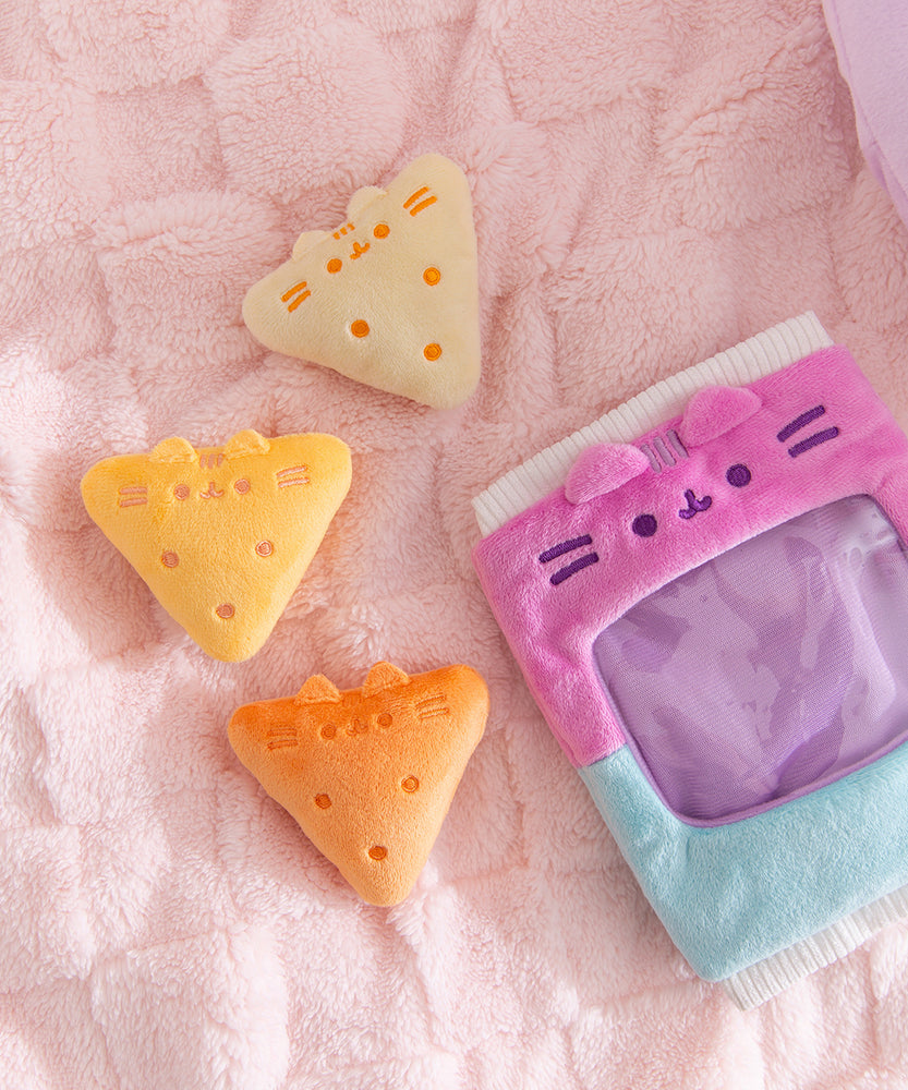Three triangle plush in a range of yellow colors sit next the the plush bag they come in. Each chip plush has Pusheen's two ears extending off the plush and three stripes embroidered between the ears.