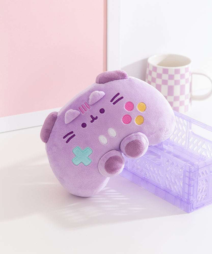 Purple Gamer Pusheen plush is propped up on a desk to show its unique shape. Pusheen the Cat's ears can be seen extending off the front of the plush. 