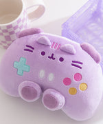 Front view of the purple gaming controller inspired plush toy that includes dark purple trigger buttons and joysticks paired with multi-colored embroidered buttons. Pusheen the Cat's face and ears are embroidered near the top of the plush. 