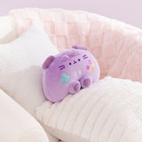 Gamer Pusheen Controller Plush sits in a chair surrounded by blankets and pillows to show the size and scale of the purple plush toy.