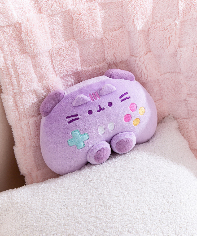 Front view of the purple gaming controller inspired plush toy that includes dark purple trigger buttons and joysticks paired with multi-colored embroidered buttons. Pusheen the Cat's face and ears are embroidered near the top of the plush. 