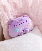 Front view of the purple gaming controller inspired plush toy that includes dark purple trigger buttons and joysticks paired with multi-colored embroidered buttons. Pusheen the Cat's face and ears are embroidered near the top of the plush. 