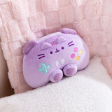 Front view of the purple gaming controller inspired plush toy that includes dark purple trigger buttons and joysticks paired with multi-colored embroidered buttons. Pusheen the Cat's face and ears are embroidered near the top of the plush. 