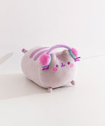 Side quarter view of the gaming squisheen. Pusheen the cat lazes while wearing a pair of multi-colored pastel headphones.