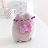 Gamer themed cat plush sits on a white desktop. The purple-hued cat holds a pink gaming controller with multi-colored buttons.