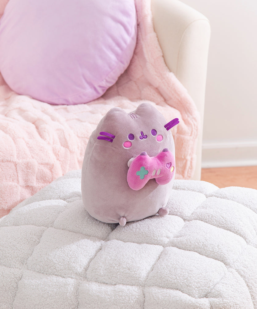 Side quarter view of the Gamer Pusheen Plush. The gray cat has a pink embroidered blush that sits under her purple eyes and mouth.