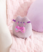 Alternate side quarter view of gamer plush. Pusheen the Cat holds a pink and purple gaming controller with a teal plus button, purple heart button, yellow circle button, and two white oblong buttons on the front of the controller.