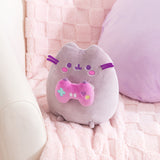 Alternate side quarter view of gamer plush. Pusheen the Cat holds a pink and purple gaming controller with a teal plus button, purple heart button, yellow circle button, and two white oblong buttons on the front of the controller.