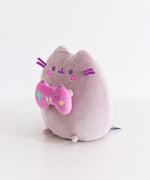 Side quarter view of the Pusheen gamer plush. Pusheen's classic three head stripes are embroidered in a light purple color between her triangle shaped 3D ears.