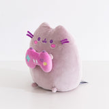 Side quarter view of the Pusheen gamer plush. Pusheen's classic three head stripes are embroidered in a light purple color between her triangle shaped 3D ears.
