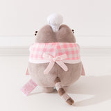 Back view of Pink Baker Pusheen Plush. The checkered top and apron combo are tied in the back with a bow. Pusheen’s gray striped tail is seen coming off the bottom back of the plush. 