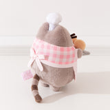 Alternate back quarter view of plush. Pusheen wearing a baking apron tied with a bow in the back while the plush stands upright on two pudgy paws. 