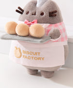 Close-up view of the apron Pusheen wears that says, “Biscuit Factory” accompanied by a cat head outline logo. 