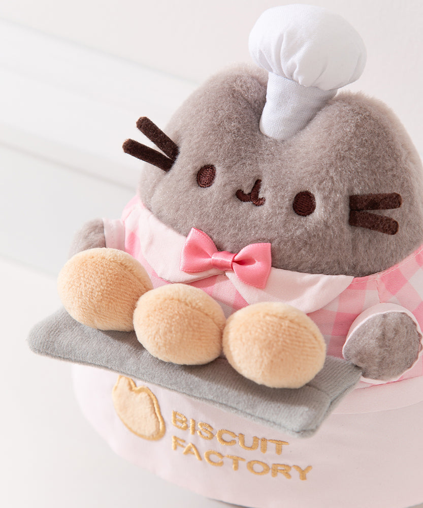 Top aerial view of Baker Pusheen plush to show off Pusheen’s three biscuit buns that are a creamy yellow color and the pink color of the tiny bow tie on the plush.