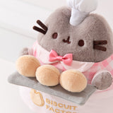 Top aerial view of Baker Pusheen plush to show off Pusheen’s three biscuit buns that are a creamy yellow color and the pink color of the tiny bow tie on the plush.