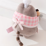 Back view of the Pink Biscuit Baker Pusheen Plush. The checkered top and apron combo are tied in the back with a bow. Pusheen’s gray striped tail is seen coming off the bottom back of the plush. 