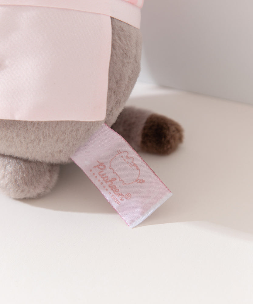 Close-up view of white and pink cggcw logo tag on the baker plush. 
