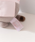 Close-up view of white and pink cggcw logo tag on the baker plush. 