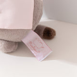 Close-up view of white and pink cggcw logo tag on the baker plush. 