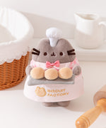 Pusheen the Cat Plush holds a tray of three fluffy golden biscuit on a gray tray.