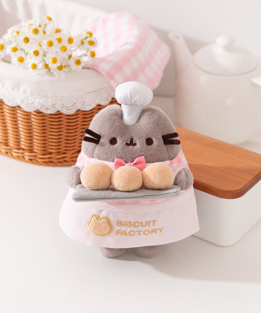 Pink Biscuit Baker Plush is a grey cat wearing a bakery outfit that's accented by pink details and white chef's hat.