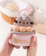 Model holding Biscuit Baker Pusheen Plush to show size scale. The sides of the plush fit in the model’s hands while the head and legs are not encompassed by the hands. 