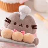 Close-up view showcasing Pusheen’s face, fuzzy coat texture, and her white patisserie chef hat that sits between her triangular ears. 