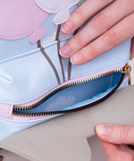 Model holds open front pocket zipper to show interior sky and clouds pattern. 