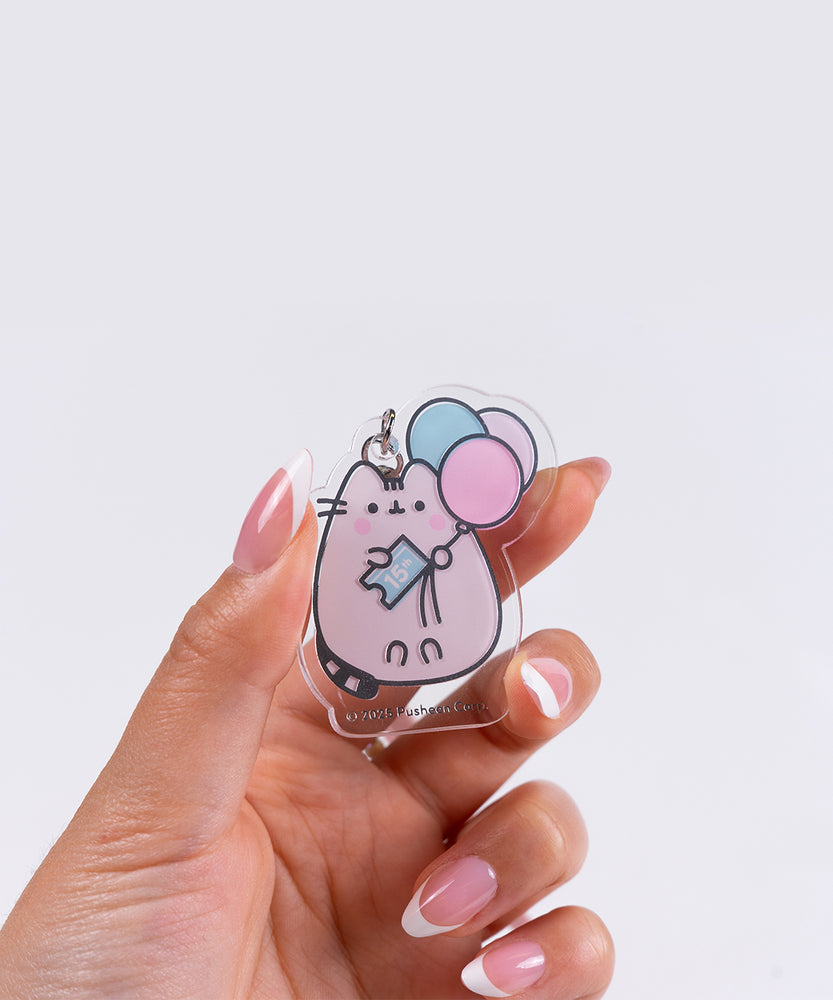 Close-up of the removable acrylic keychain of Pusheen the Cat holding a blue ticket that says "15th".