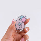 Close-up of the removable acrylic keychain of Pusheen the Cat holding a blue ticket that says "15th".