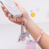 Model holds phone with attached Pusheen 15th Anniversary Beaded Phone Charm. The beaded string includes white, purple, and clear round beads, purple bow beads, and white star beads. At the end of the string is an acrylic charm of Pusheen the Cat holding a carnival ticket and three pastel balloons. 
