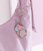 Flat ring keychain depicting Pusheen the cat with three pastel balloons hangs off a purple purse. 