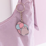 Flat ring keychain depicting Pusheen the cat with three pastel balloons hangs off a purple purse. 