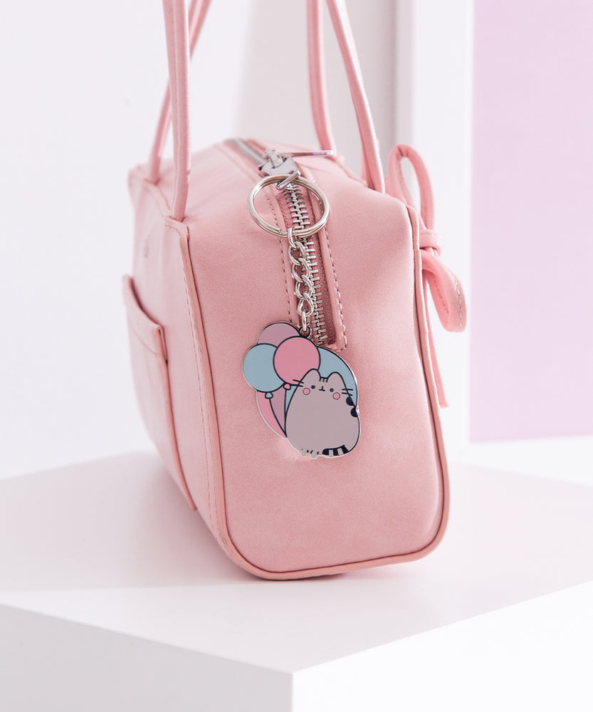 Silver pusheen keychain hangs off a pink zipper purse to show size and scale of the cat keychain. 