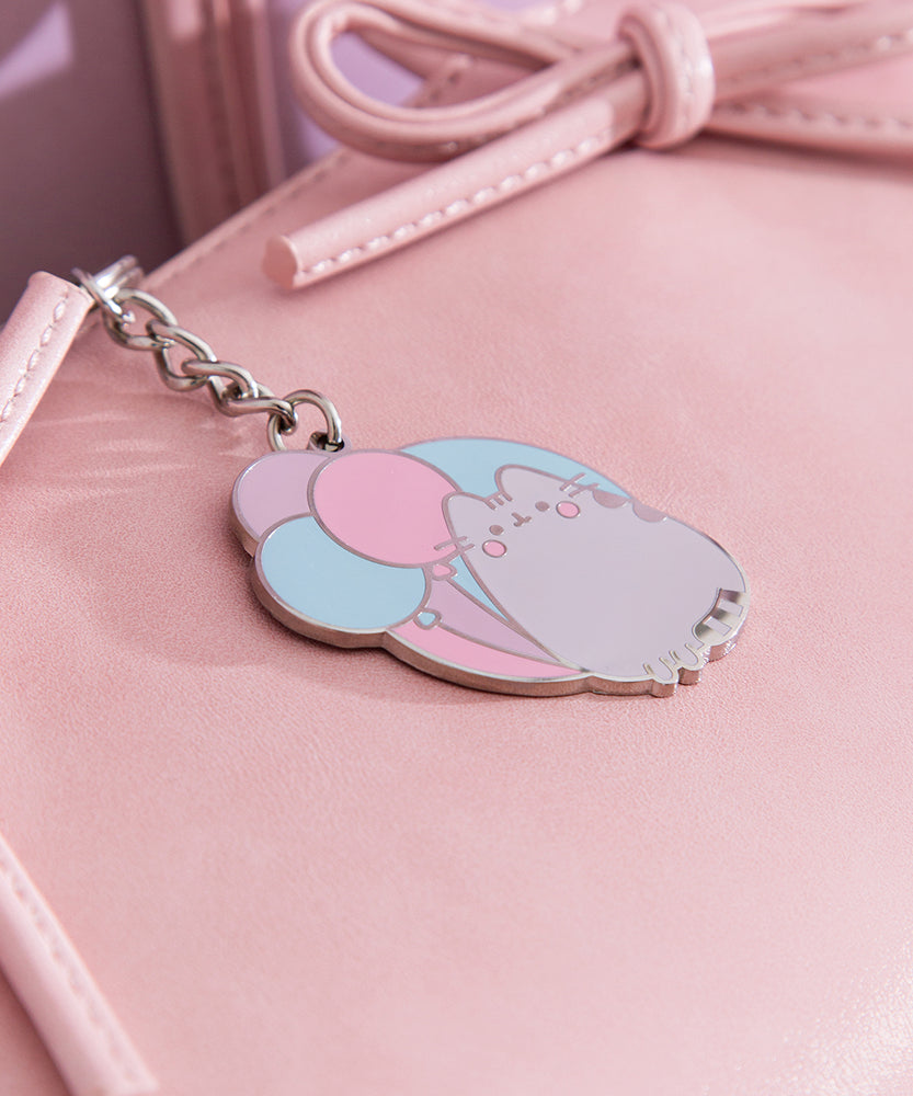 Silver 15th anniversary keychain lies flat on a pink purse to show the reflective finish of the cat.