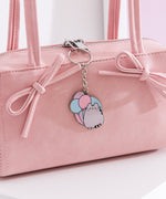 Pusheen balloon keychain hangs off the zipper of a pink purse. The cat keychain is outline in a shiny silver color. 