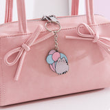 Pusheen balloon keychain hangs off the zipper of a pink purse. The cat keychain is outline in a shiny silver color. 