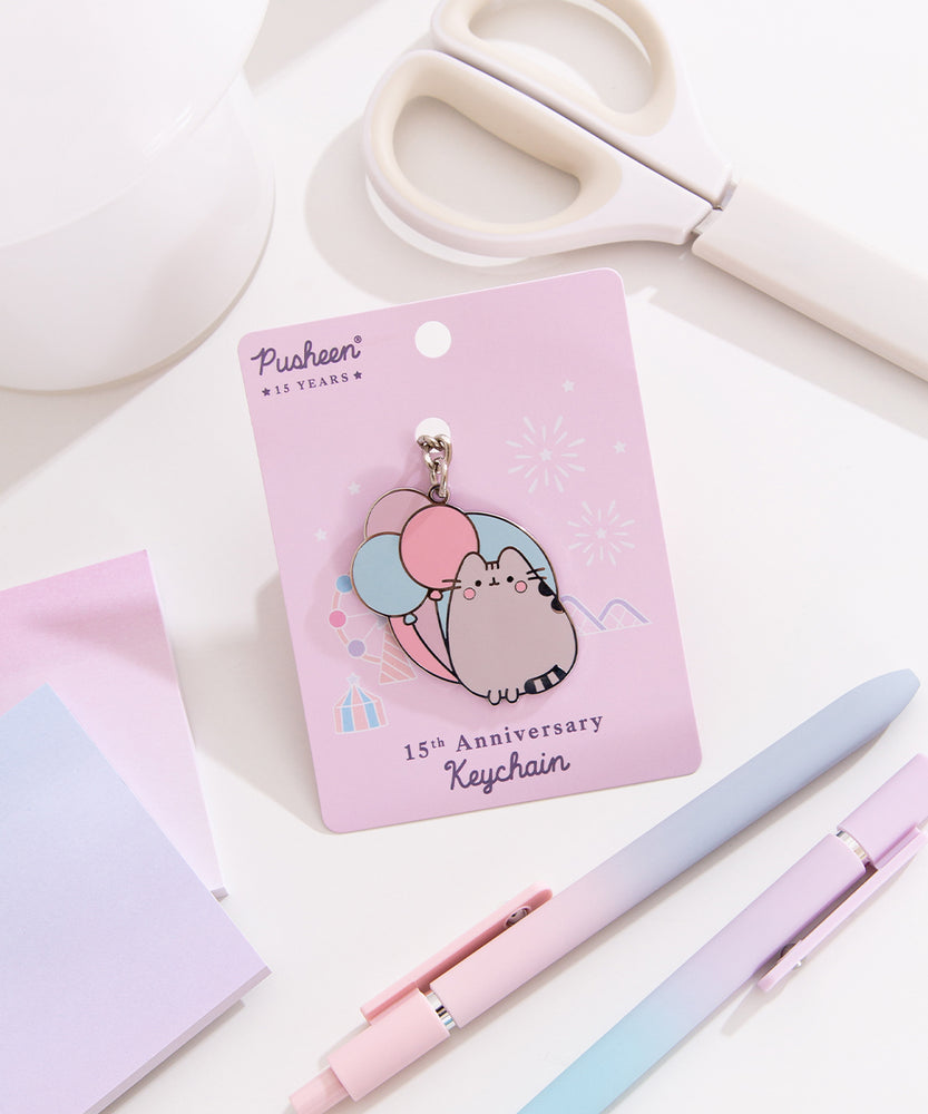 Pusheen 15th anniversary shiny nickel keychain attached to its light purple backer card. The background shown on the paper card is of a festival scene with fair rides.
