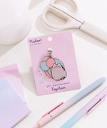Pusheen 15th anniversary shiny nickel keychain attached to its light purple backer card. The background shown on the paper card is of a festival scene with fair rides.