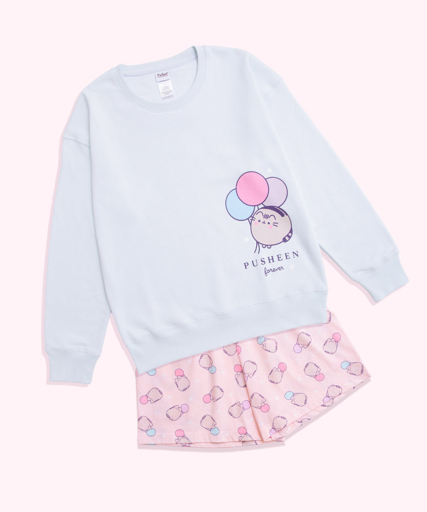 Light blue sweatshirt with Pusheen the Cat character printed on the wearer's left side. The pink shorts in the set have an all over print of Pusheen with pastel balloons. 