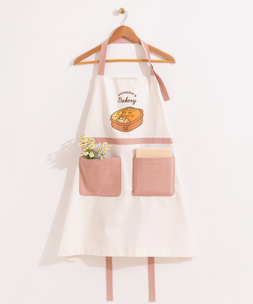 White and dusty pink apron hangs on a clothing hanger. A bundle of flowers and a notebook are placed in the oversized pink pockets on the front of the apron.