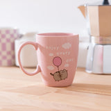 Pink Pusheen Enjoy Every Day Mug shows Pusheen the Cat floating in the white fluffy clouds with the phrase 'enjoy every day'.