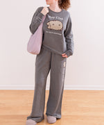 Model wearing Pusheen Loungewear Set. The grey outfit includes a sweatshirt and matching pants. The model is carrying a purple purse.