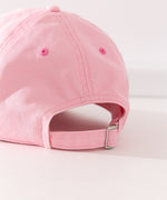 Close-up view of the buckle adjustment strap on the back of the cap. The buckle strap hat seams matches the light pink color hat color while the eyelet holes are a slightly darker pink color.  