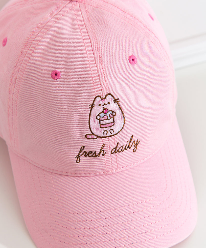 Fresh Daily Pusheen Sweets pink cap. The cat holds a cherry tiered mini cake. 