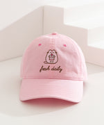Pusheen Sweets Cap on a white surface. The light pink cap features Pusheen the Cat in a pink hue while outlined by a dark brown color. The phrase "fresh daily" sits below the cat embroidery. 
